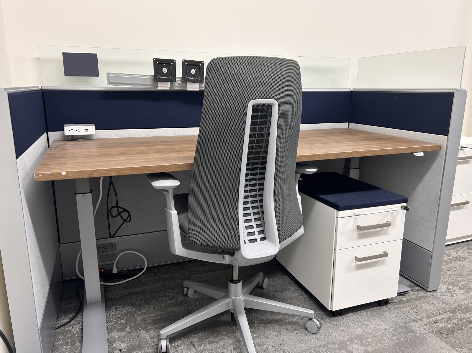 A workstation with navy fabric panels, a glass-topped partition, and a rolling storage pedestal