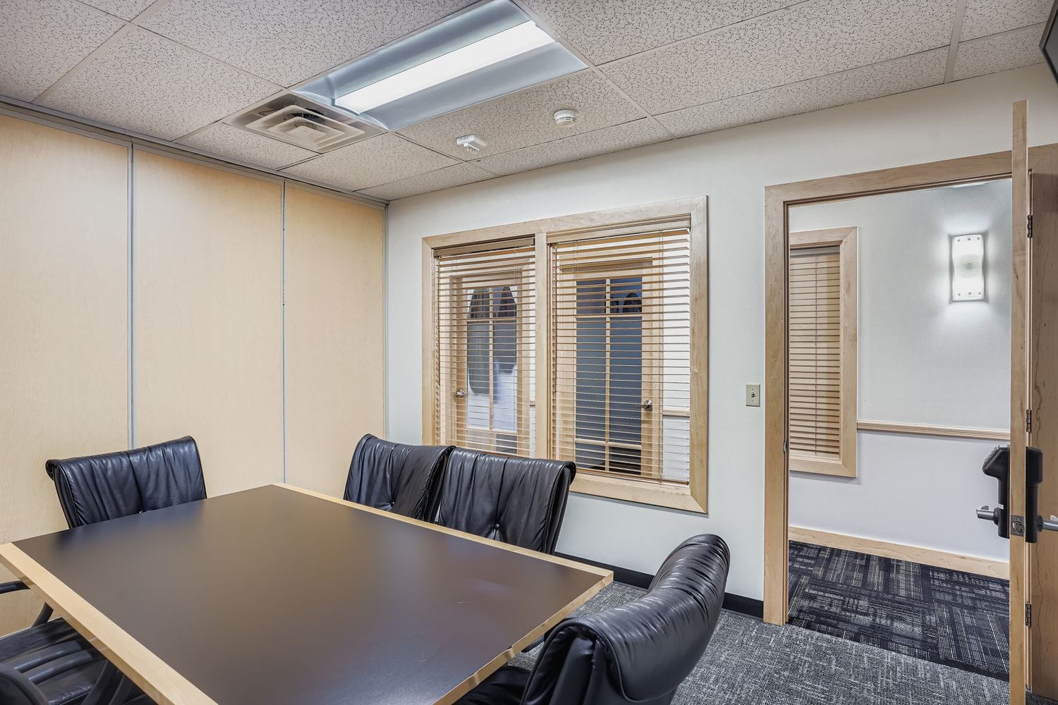 Modern office meeting room with black leather chairs, wooden accents, and natural light.