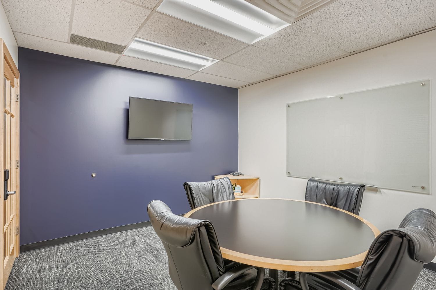 Modern office conference room with seating, whiteboard, and TV for professional meetings and virtual collaboration.