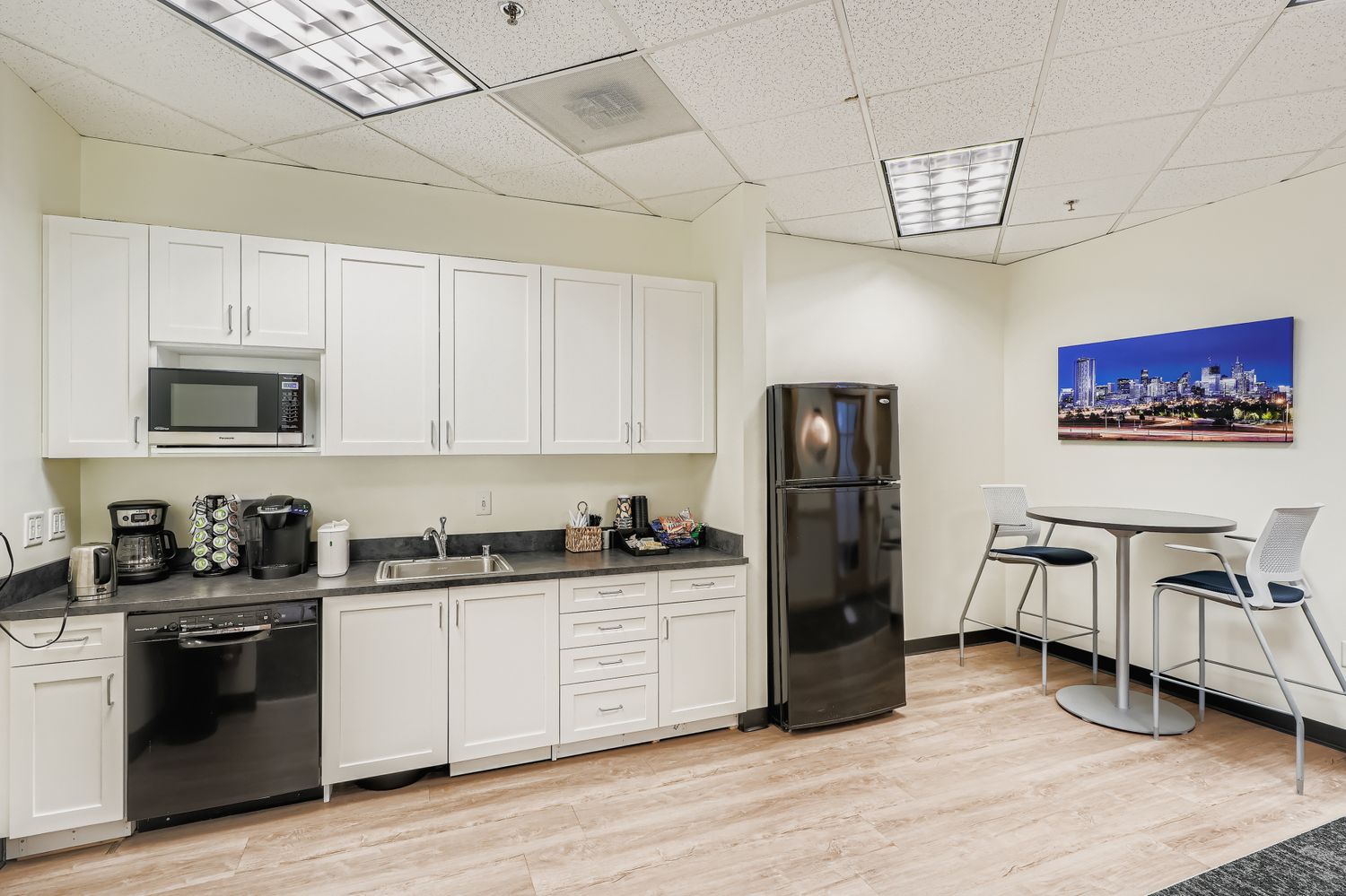 Modern office kitchen with coffee station and seating area for productive work environment.