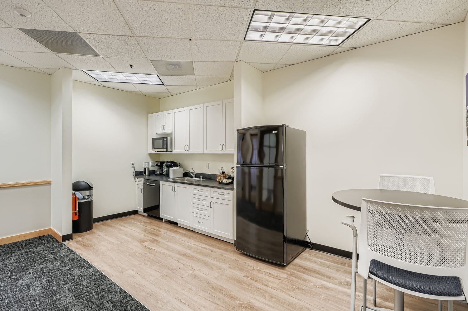 Modern office kitchenette with coffee machine and refrigerator for business amenities.