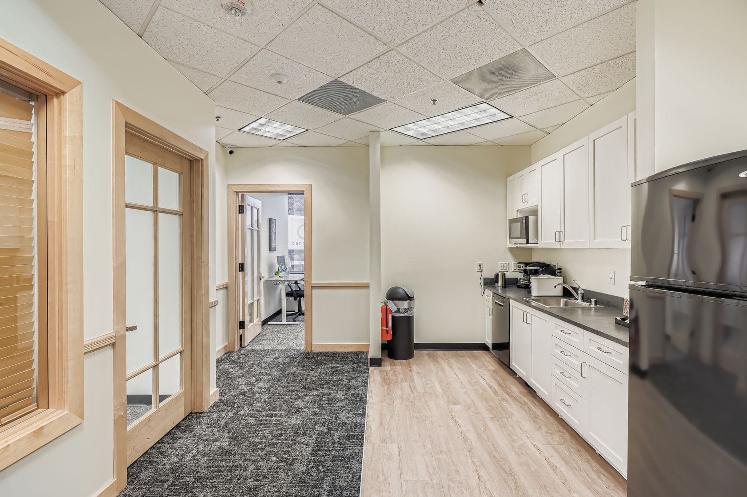 Modern office kitchenette with white cabinets, coffee station, and meeting rooms at Intelligent Office.