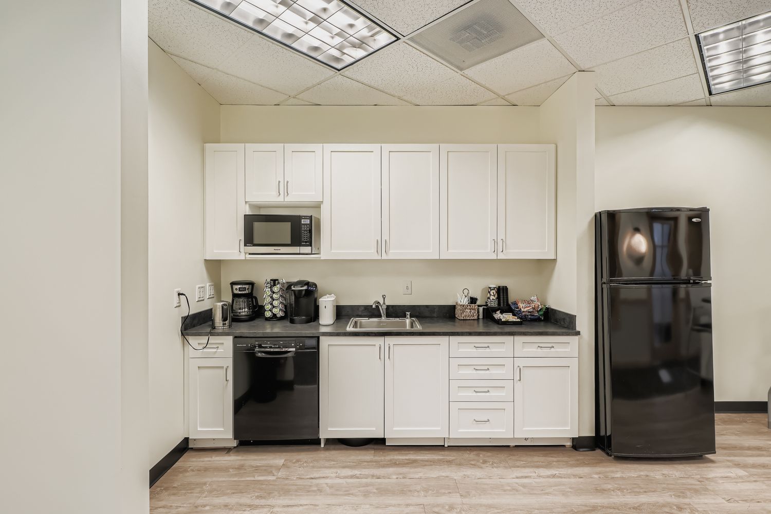Microwave and coffee station in modern office break room with white cabinets.