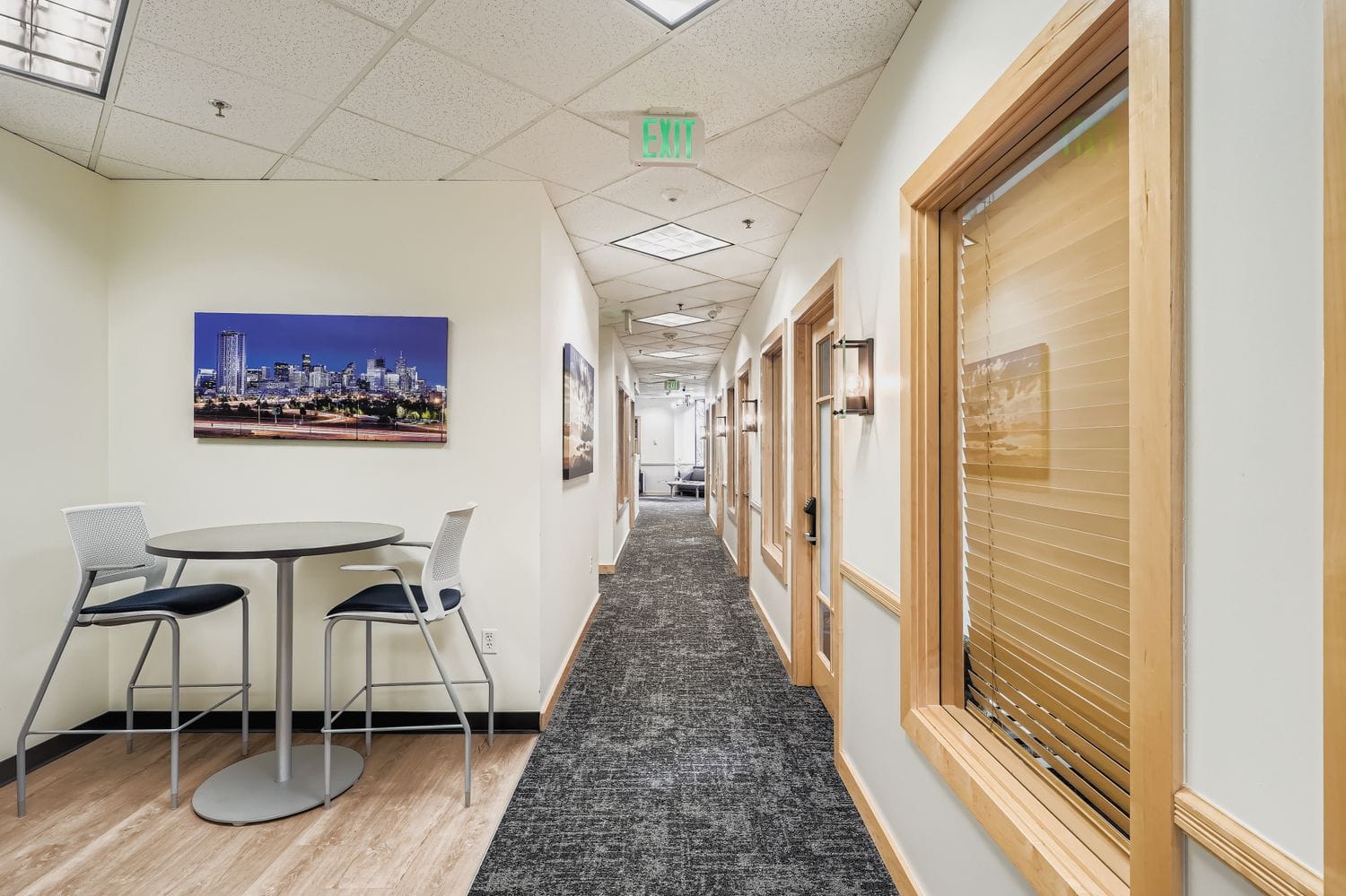 Modern office hallway with private offices and lounge area, featuring natural wood accents and contemporary lighting.