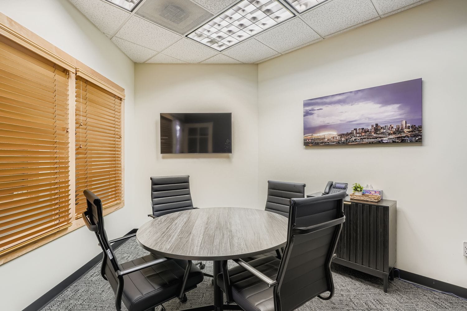 Comfortable executive meeting room with modern decor, flat-screen TV, and city skyline art.