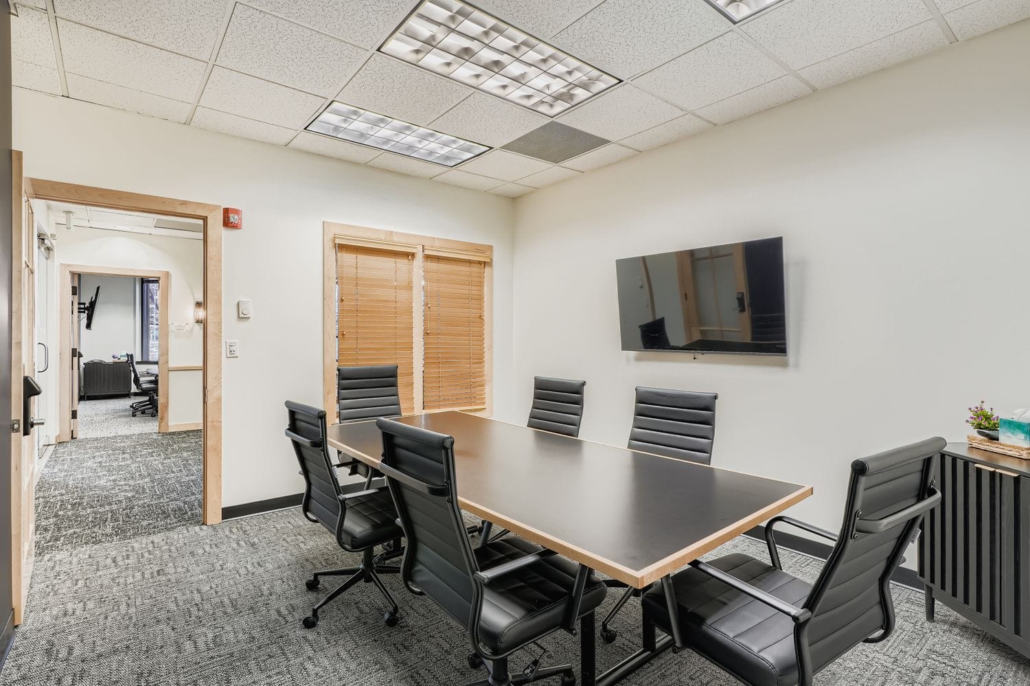 Modern office conference room with black chairs and wall-mounted TV, ideal workspace solution.