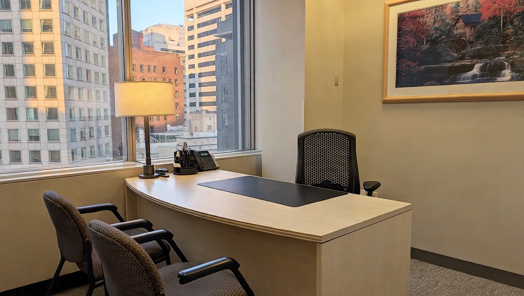 Modern office workspace with a large window and city view, featuring a sleek desk and comfortable chairs for professional meetings.