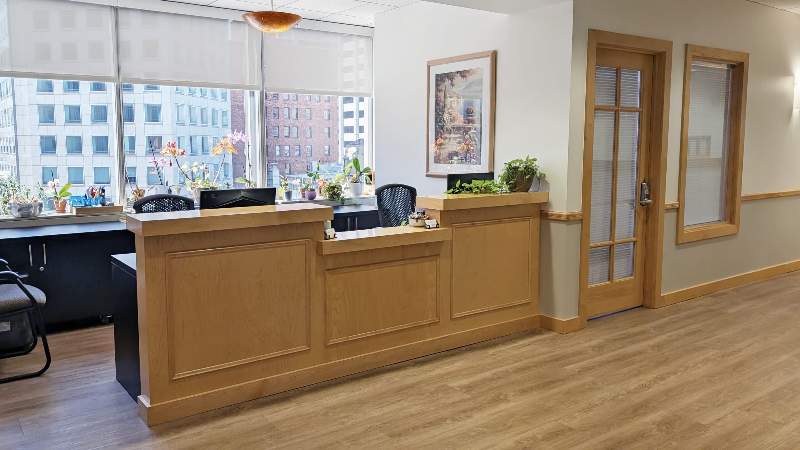 Bright office reception area with wooden accents, potted plants, and large windows, showcasing modern workplace design and professional environment.