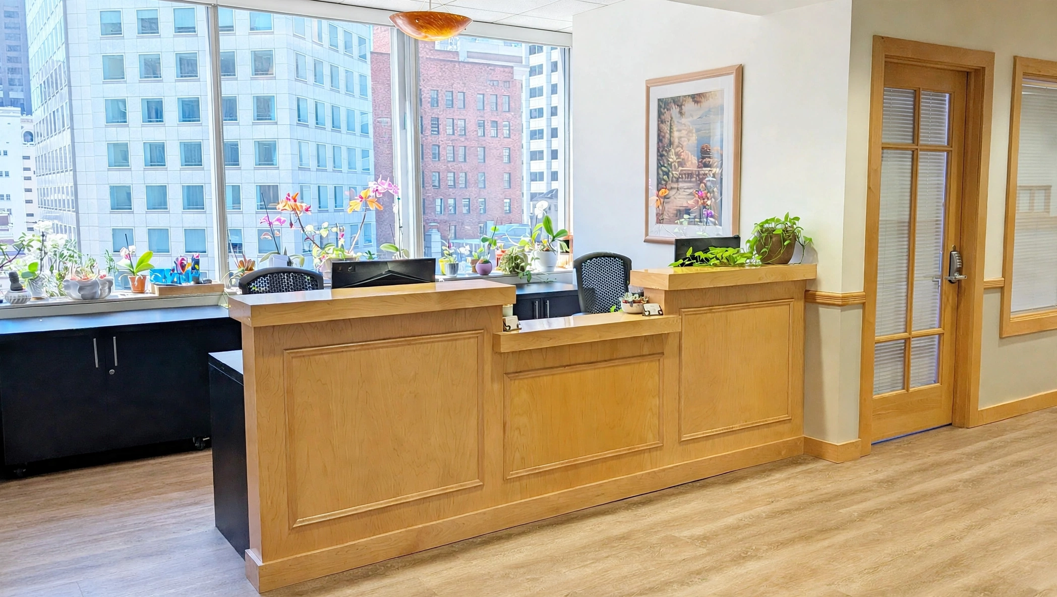 Bright office reception area with wooden accents, potted plants, and large windows, showcasing modern workplace design and professional environment.