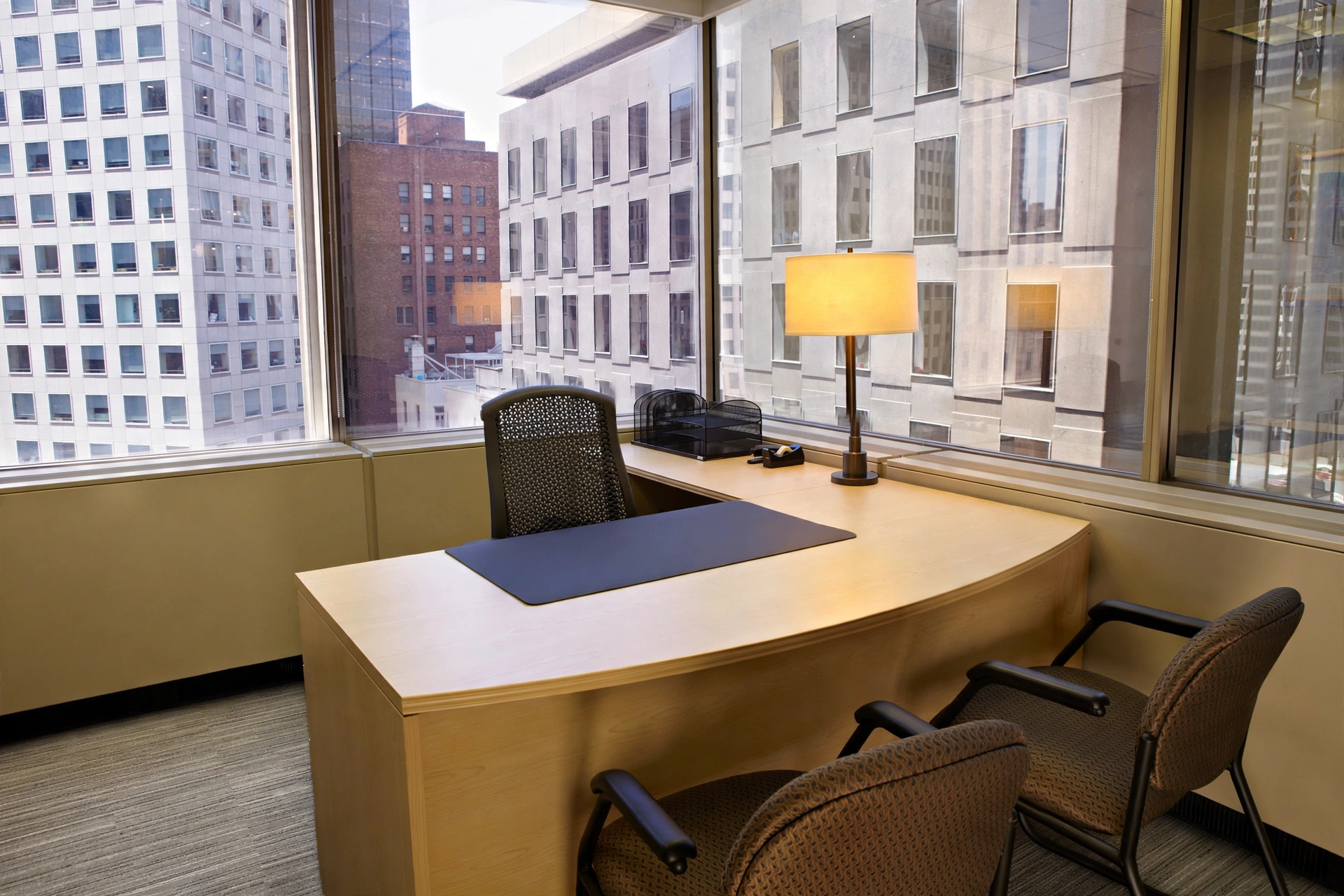 Modern office workspace with large city views, furnished with a wooden desk, chairs, and essential office equipment.
