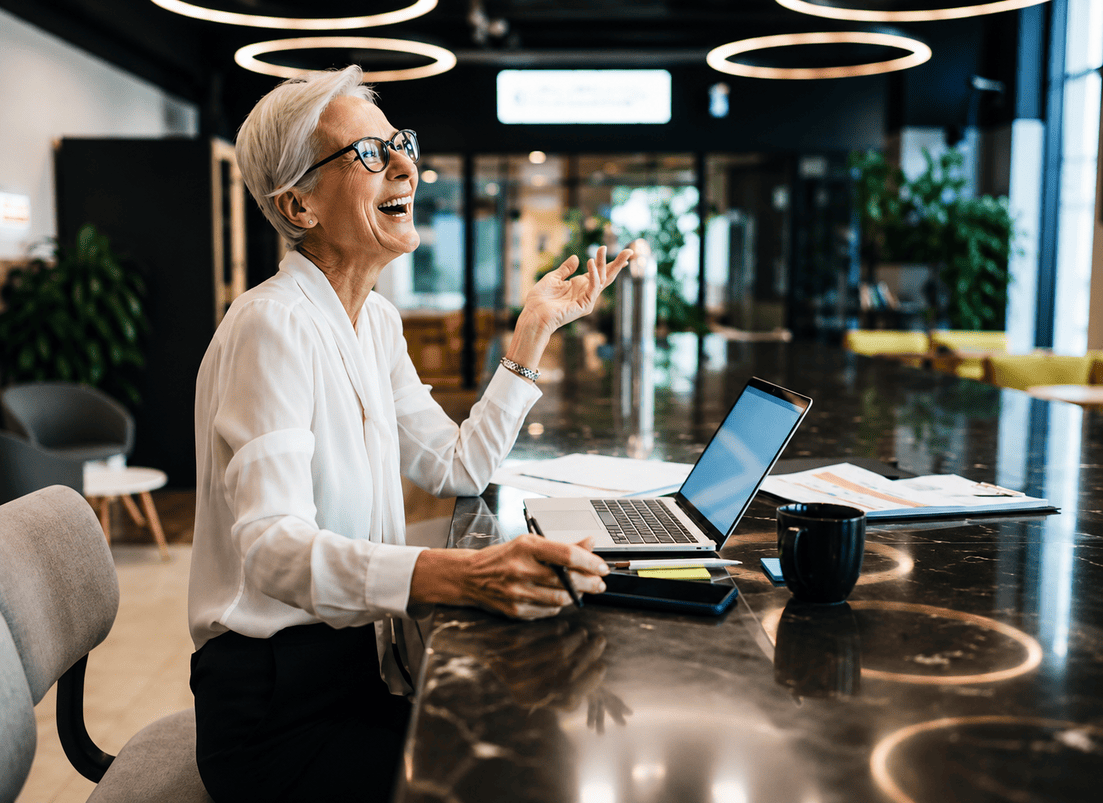 Professional woman smiling while working on a laptop in a modern office workspace.