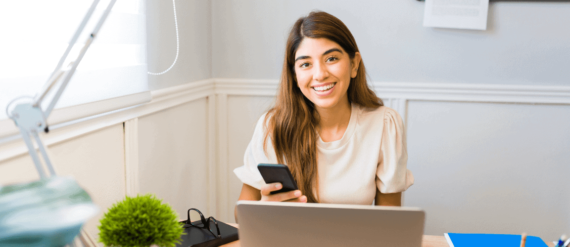 Bright young woman working at a modern coworking space with laptop and smartphone for professional business solutions.