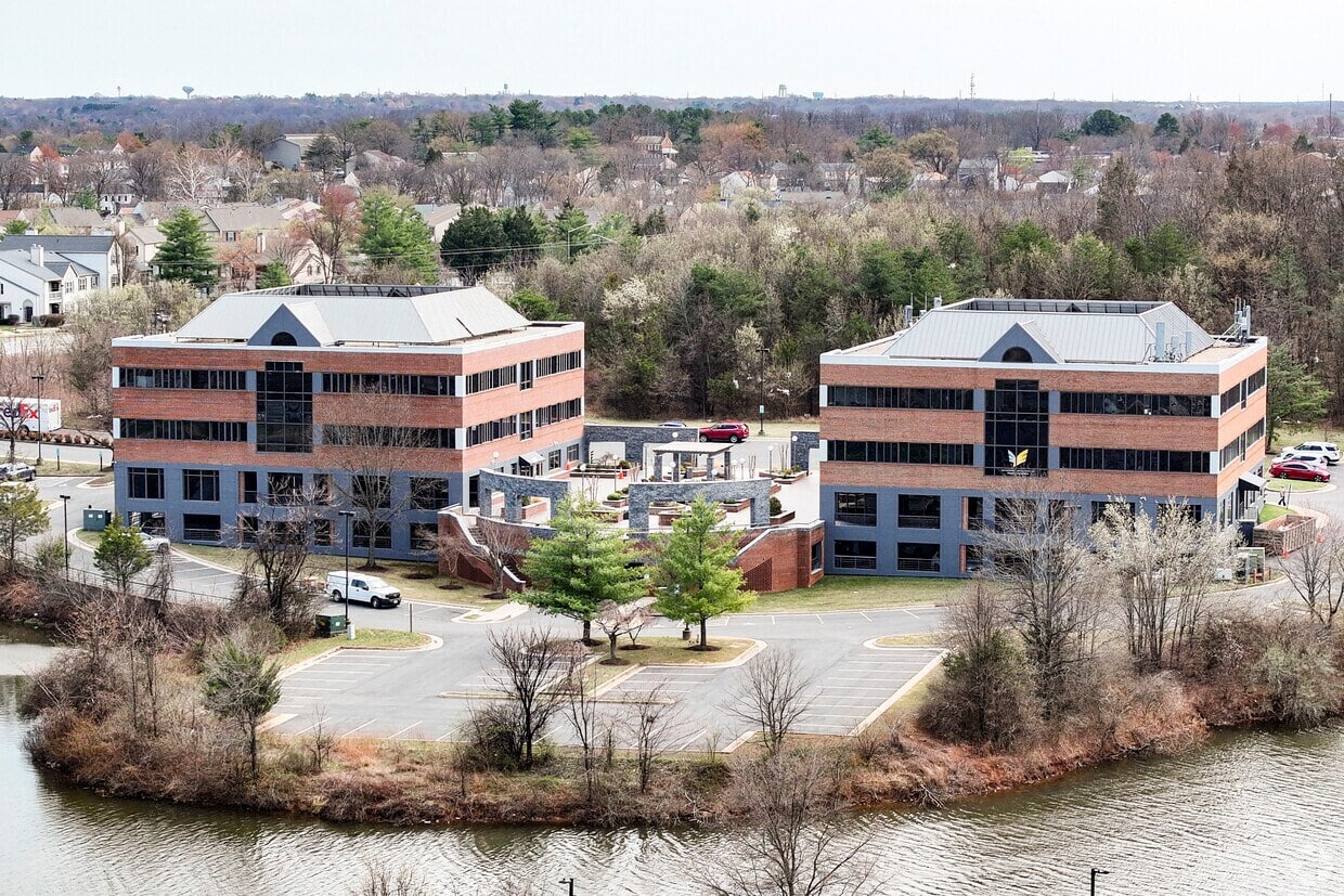 Office buildings near water with trees and parking lot.