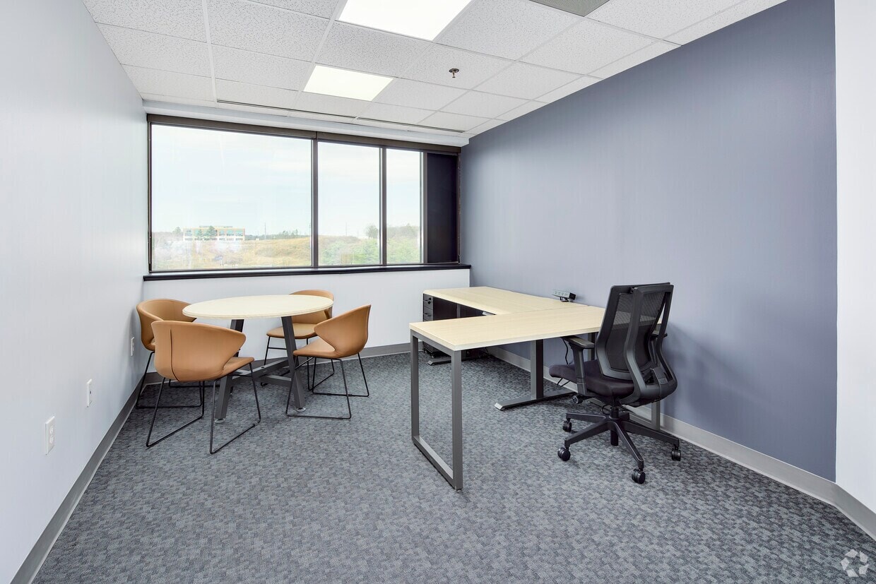 Office workspace with large window, desk, and seating area for meetings or work.