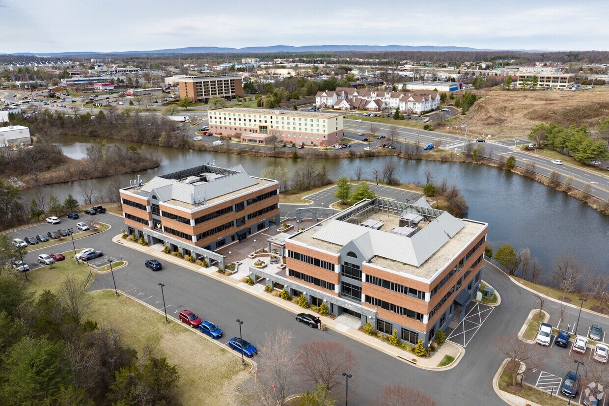 Modern office buildings near a water body with parking lot and surrounding landscape.