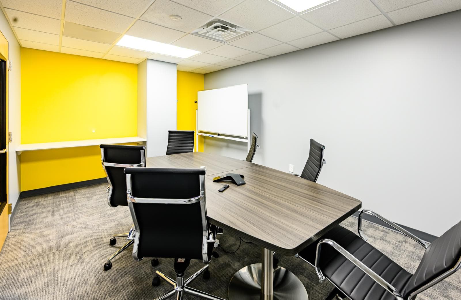 Office meeting room with a large table, black chairs, and a whiteboard, featuring a vibrant yellow w.
