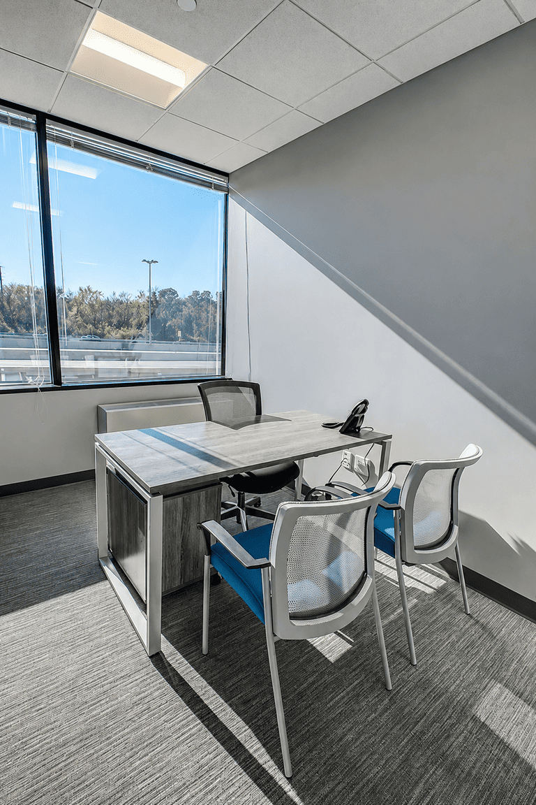 Modern private office with desk, guest seating, large window, and natural light.